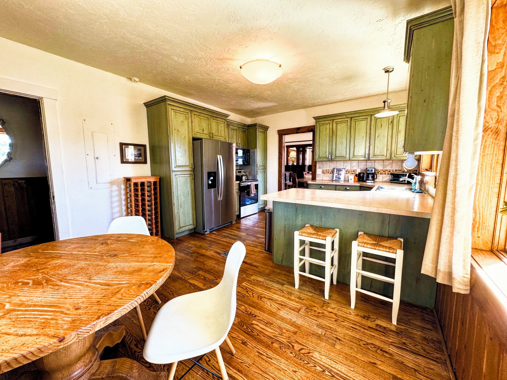 Una cocina con armarios de madera, un refrigerador, una mesa de comedor con sillas y una pequeña isla con taburetes.