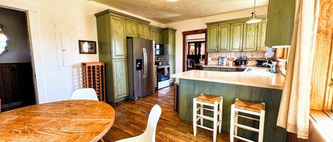 Una cocina con armarios de madera, un refrigerador, una mesa de comedor con sillas y una pequeña isla con taburetes.