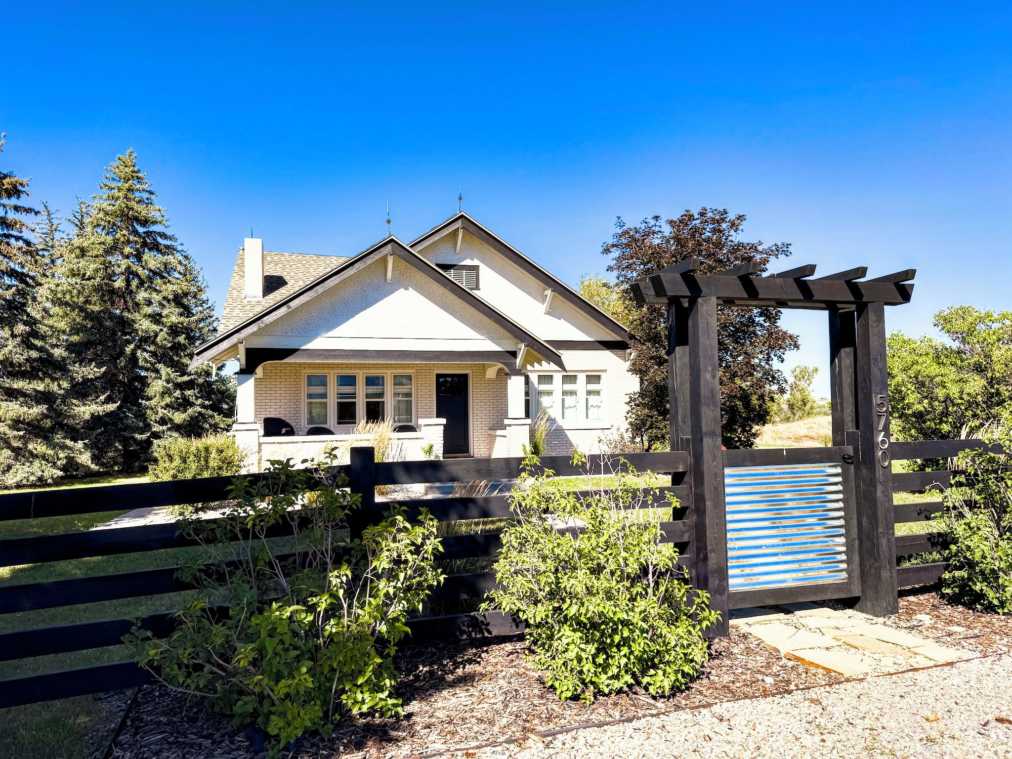 A house with a front porch, a wooden fence, and a pergola with a blue and white striped awning.