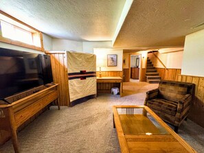 A cozy living room with a television, wooden furniture, a staircase, and a framed picture on the wall. - 5-Bedroom Craftsman Farmhouse With Teton Views (Tetonia)