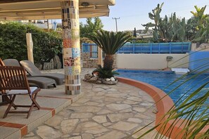 Ein Poolbereich mit einer Mosaiksäule, Liegestühlen und einem Boden aus Steinplatten.