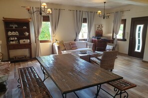 Ein Essbereich mit Holztisch und Bänken, einer Couch und einem Bücherregal mit Küchenutensilien.