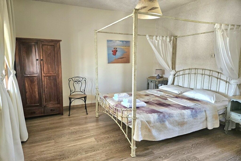 A four-poster bed with a canopy, a wooden wardrobe, a small chair, and a painting on the wall.