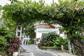 Una entrada principal del complejo con un arco de madera, una escalera que sube y abundante vegetación.