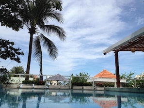 Una piscina con cielo despejado, palmeras y un edificio con techo rojo.