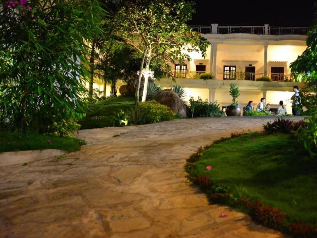 A stone pathway leading to a building with a pool and a well-maintained garden at night.