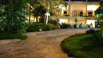 A stone pathway leading to a building with a pool and a well-maintained garden at night.