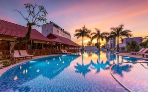Una piscina con sillones de descanso, palmeras y edificios con techos de tejas rojas.