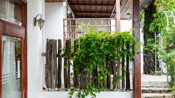 A covered outdoor seating area with two wooden chairs and a table, a bamboo ceiling, and a wall with climbing plants.