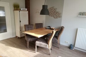 A dining area with a wooden table, cushioned chairs, a pendant light, and a radiator. - Holiday apartment with 1 bedroom (Westerland)