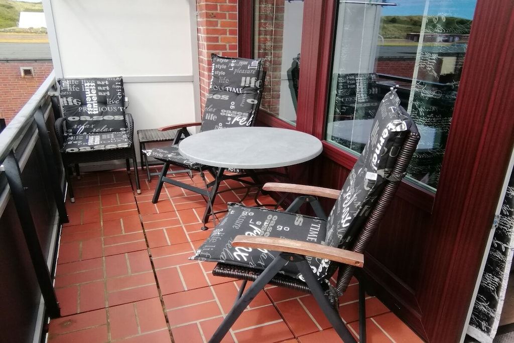 A small outdoor seating area with a round table and two chairs, one with a cushion.