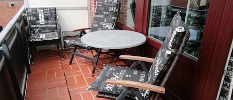 A small outdoor seating area with a round table and two chairs, one with a cushion.