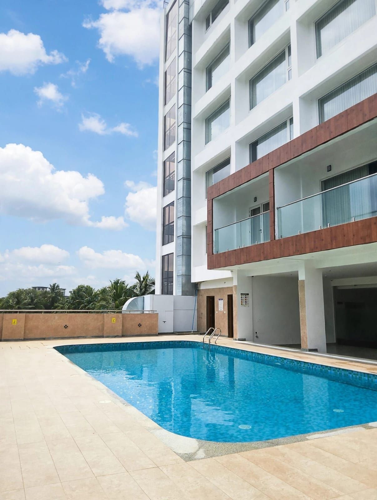 A modern building with a swimming pool, multiple balconies, and a clear sky.