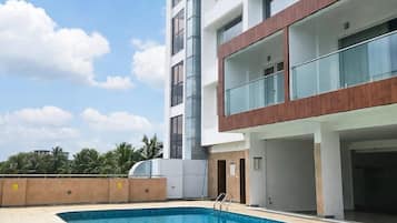 A modern building with a swimming pool, multiple balconies, and a clear sky.