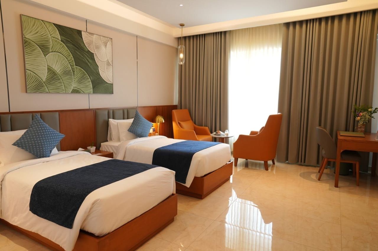 A hotel room with two beds, a desk, a chair, and a large window with curtains.