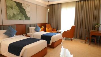 A hotel room with two beds, a desk, a chair, and a large window with curtains.