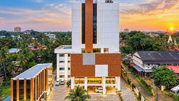 A modern building with a central tower, surrounded by greenery and other structures.