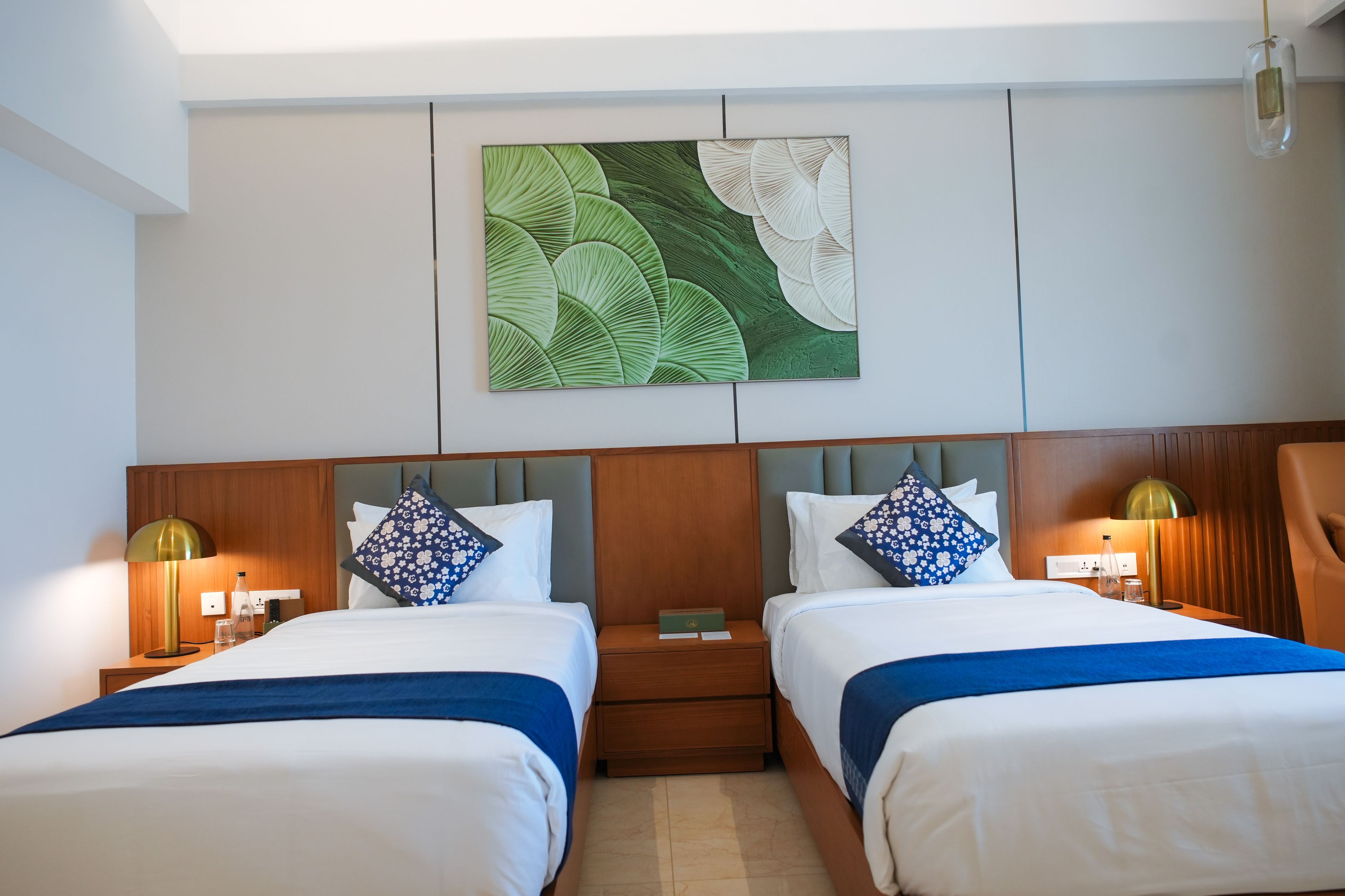 A hotel room with two beds, a nightstand, a lamp, and a wall art piece.