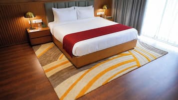 A hotel room with a large bed, wooden headboard, two bedside lamps, a red throw blanket, and a patterned rug.