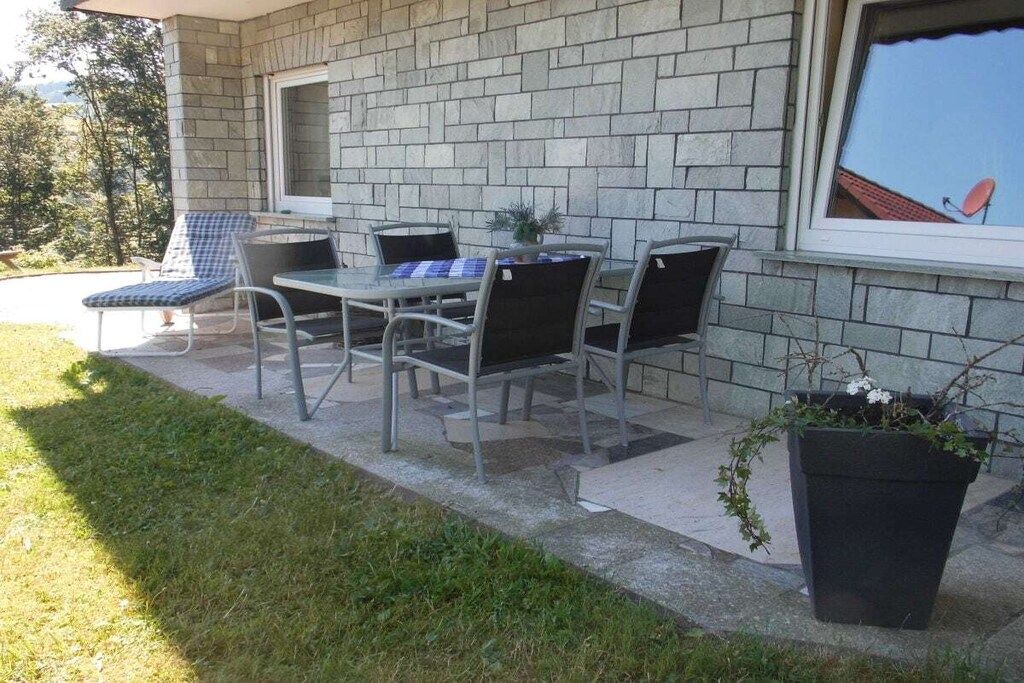 An outdoor patio with a table and chairs, a potted plant, and a window with a view of the sky.