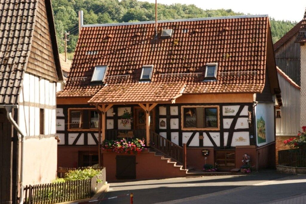 A traditional half-timbered building with a sloped tiled roof, a front porch with flower boxes, and a small staircase leading to the entrance.
