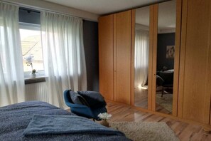 Een slaapkamer met een bed, een raam met gordijnen, een kledingkast en een stoel.