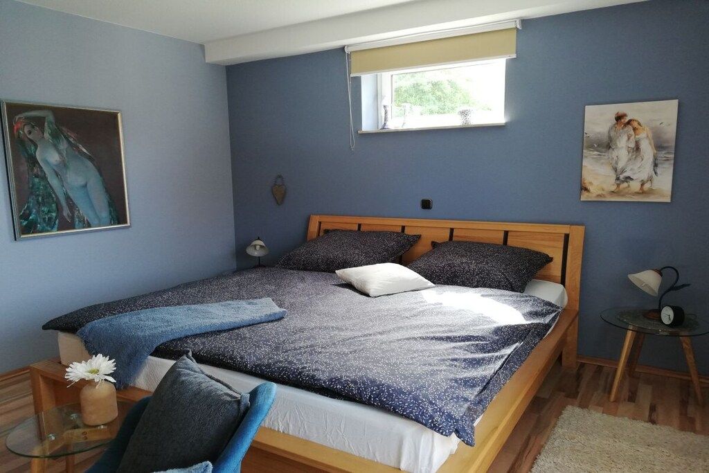 A bedroom with a bed, a bedside table, a window, and artwork on the walls.