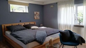 Une chambre à coucher avec un lit, une chaise, une fenêtre avec des rideaux et une lampe fixée au mur.