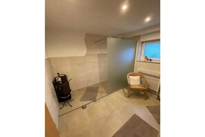 A bathroom with a shower, a chair, and a window. - Holiday apartment with 1 bedroom (Flörsbachtal-Lohrhaupten)