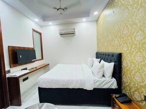 A hotel room with a bed, a television, an air conditioning unit, a wooden bedside table, and a patterned wall.