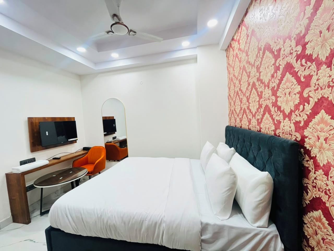 A hotel room with a bed, a desk, a chair, a television, and a ceiling fan.