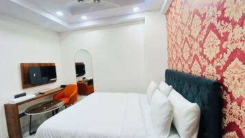 A hotel room with a bed, a desk, a chair, a television, and a ceiling fan.