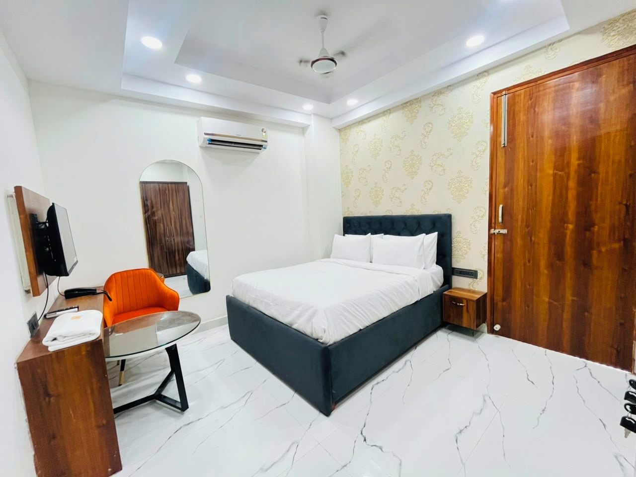 A hotel room with a bed, a desk, a chair, a wardrobe, and a mirror.