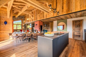 A rustic interior with exposed wooden beams, a dining area with chairs and a table, and a kitchen with a large island. - Chalet Haute Cime - Les Gets - Les Cornuts (Les Gets)
