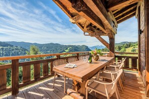 Une terrasse en bois avec une table et des chaises, d’où l’on peut admirer un paysage montagneux.