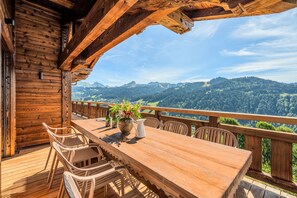 Une terrasse en bois avec une table et des chaises, offrant une vue sur un paysage montagneux.