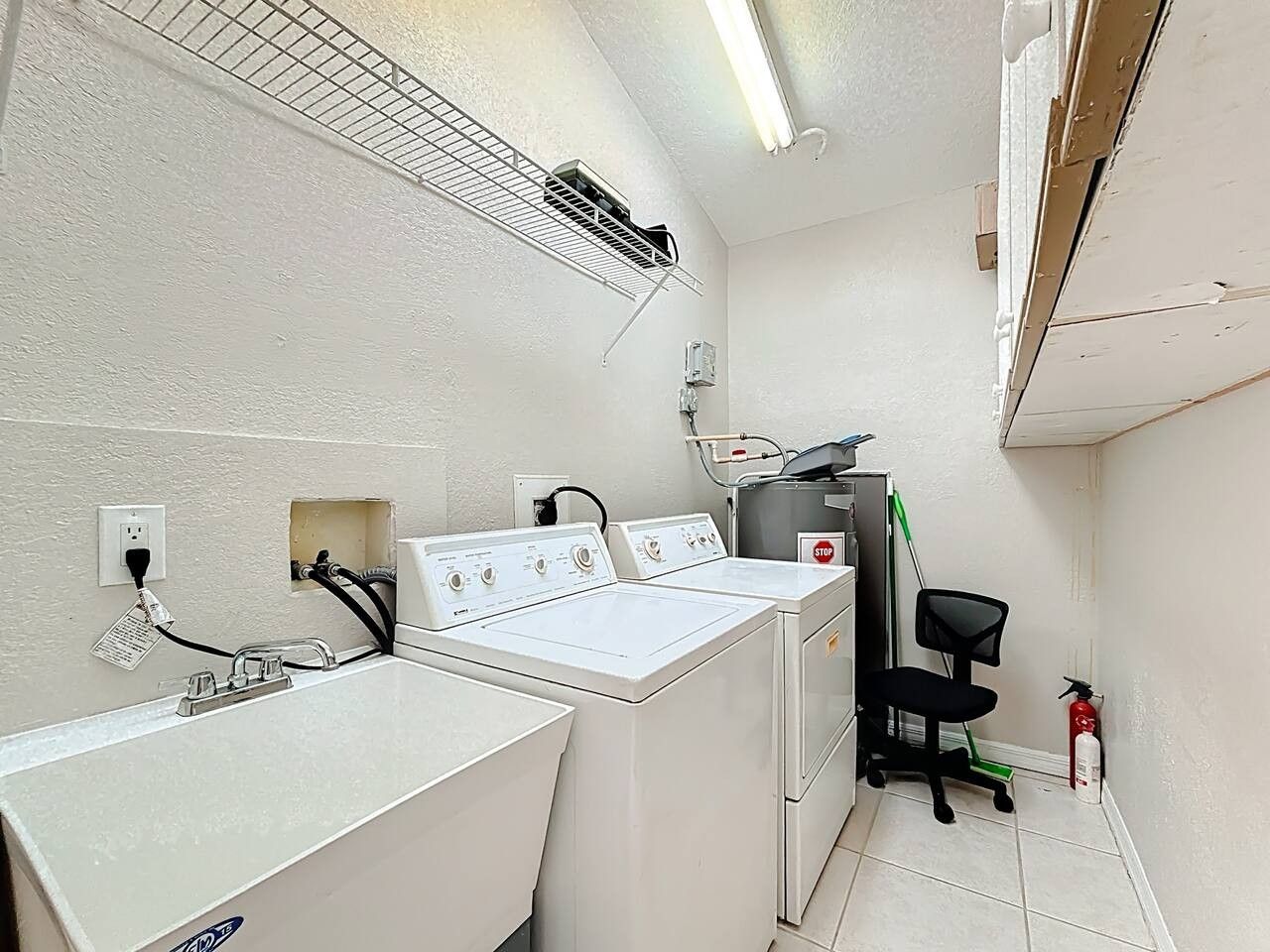 A laundry room with a washing machine, dryer, and a small office chair.