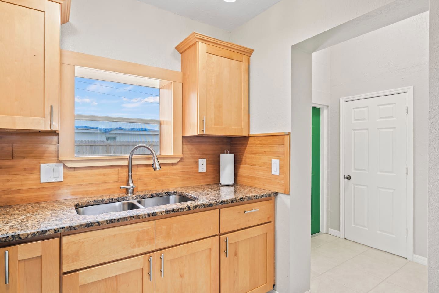 A kitchen with wooden cabinets, a granite countertop, a stainless steel sink, and a window with a view.