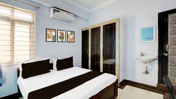 Ein Hotelzimmer mit einem Bett, einer Klimaanlage, einem Fenster mit Jalousien, einer Tür und einem wandmontierten Waschbecken.