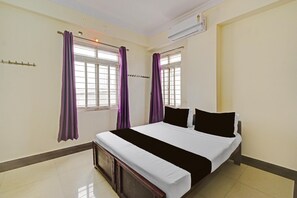 A room with a bed, two windows with purple curtains, an air conditioning unit, and a tiled floor. - Deluxe Room Sunidh (Hyderabad)