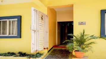 A yellow building with a white door, a window, and a potted plant.