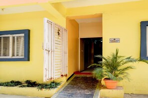 Un edificio amarillo con una puerta blanca, una ventana y una planta en maceta.