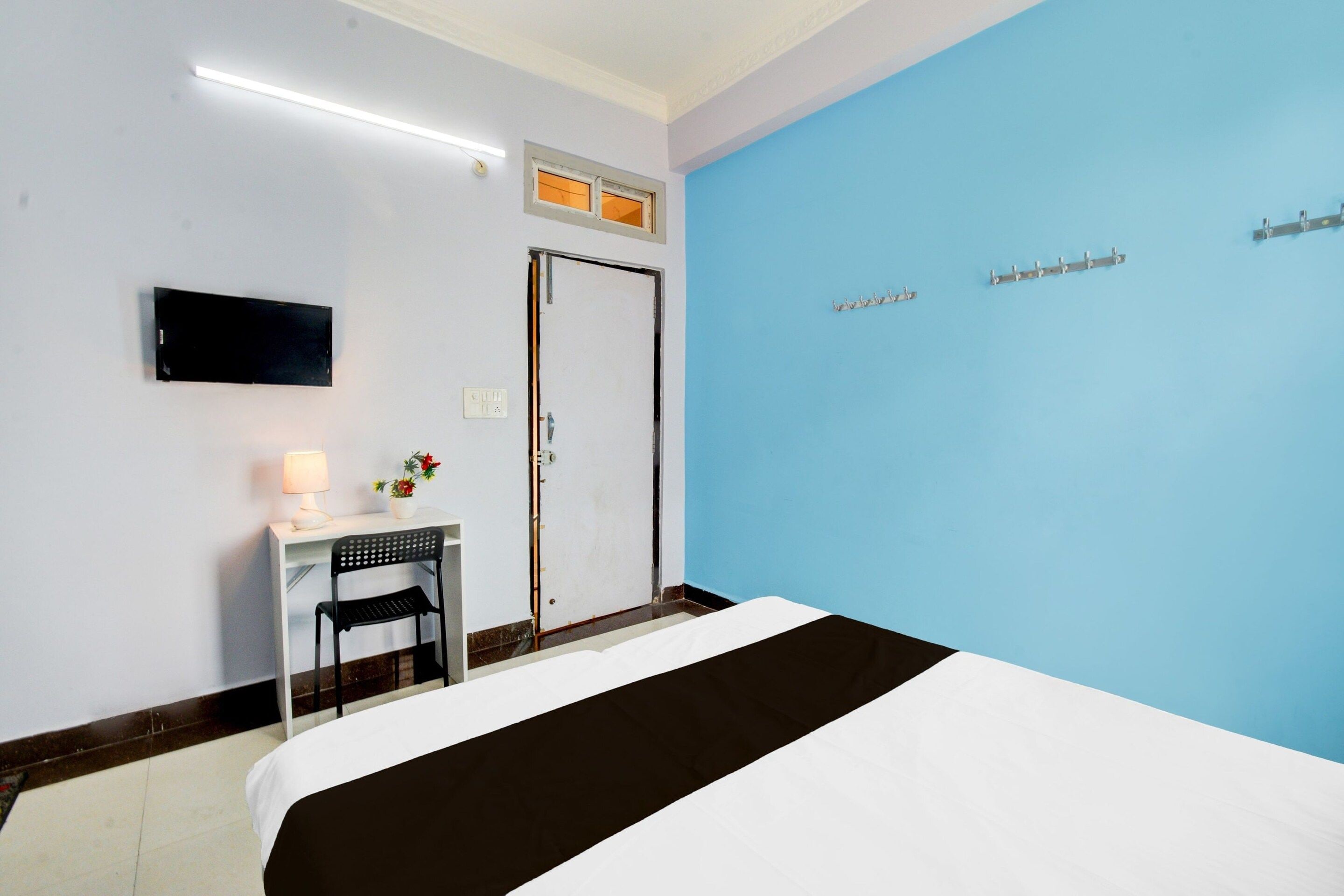 A hotel room with a bed, a desk with a chair, a television, and a blue accent wall.