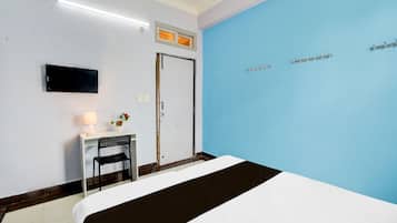 A hotel room with a bed, a desk with a chair, a television, and a blue accent wall.