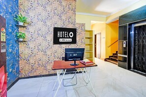 A hotel reception area with a sign indicating it is serviced by OYO. There is a desk with a computer and a chair, a plant on the left, and a staircase to the right. - Deluxe Room Sunidh (Hyderabad)