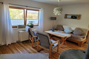 Een gezellige woonkamer met een houten vloer, een bank, een eettafel en een raam met gordijnen.