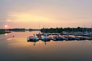 Un port de plaisance où des bateaux sont amarrés sur une eau calme, au coucher du soleil.