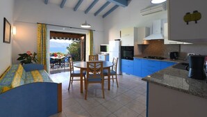 Cozinha moderna com armários azuis, área de jantar com mesa e cadeiras, e vista para o exterior.
