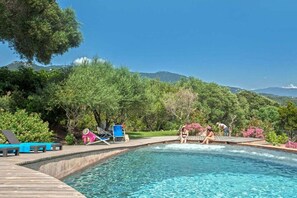 Une piscine dotée d’une terrasse en bois, entourée d’une végétation luxuriante et d’arbres.