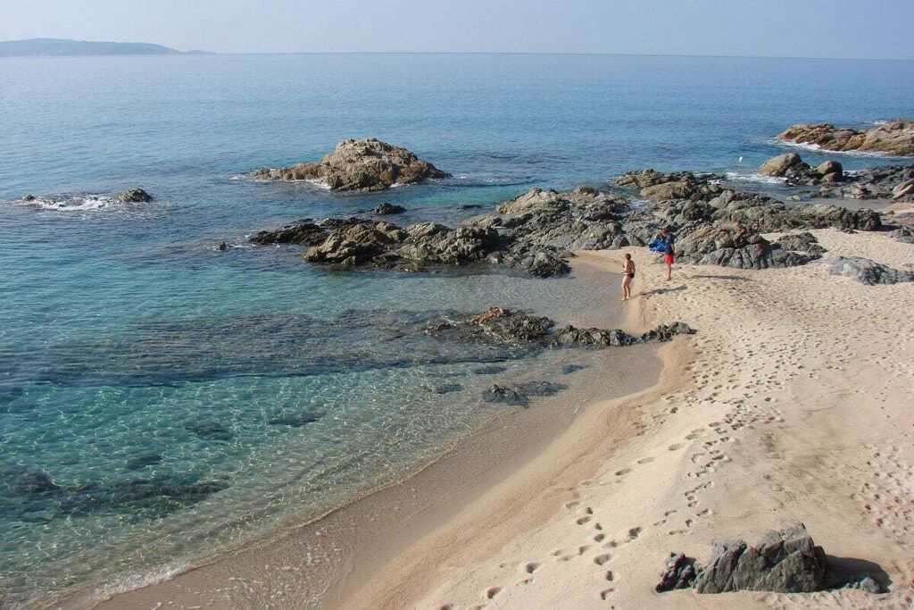 Una playa con aguas transparentes, afloramientos rocosos e huellas.